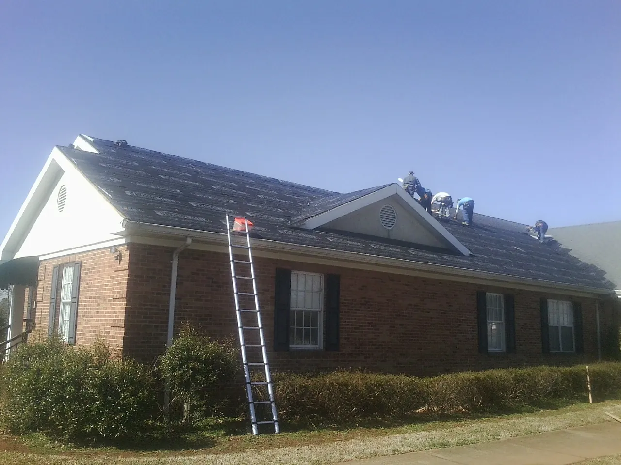 Crew tearing shingles off a brick ranch roof with a ladder set — Emergency Roof Repair work by our crew in Wood River