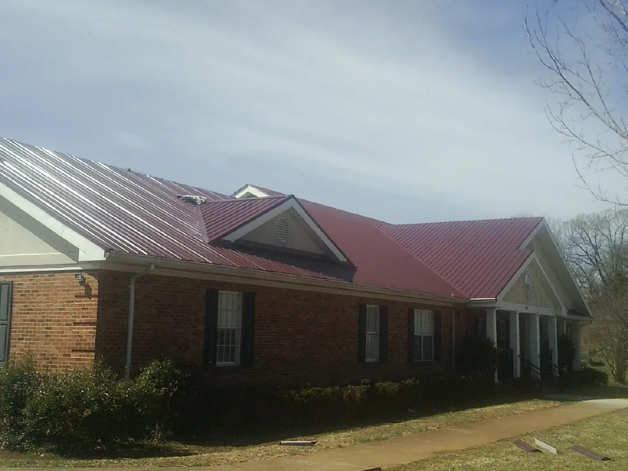 Red metal roof with gabled entries on a long brick building, from a Hail Damage Roof Repair job in Wood River