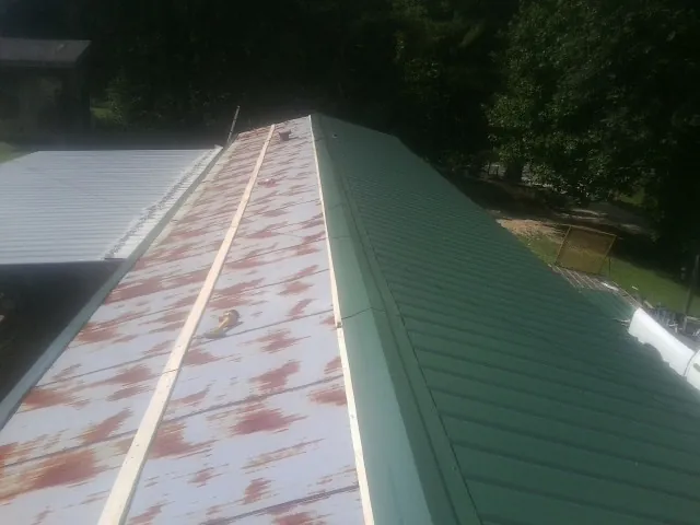 Old rusted panels beside newly installed green metal roofing in Wood River