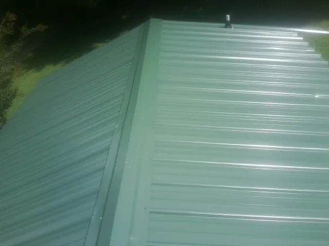 New green metal panels meeting at the ridge of a roof — Flat Roof Repair work by our crew in Wood River