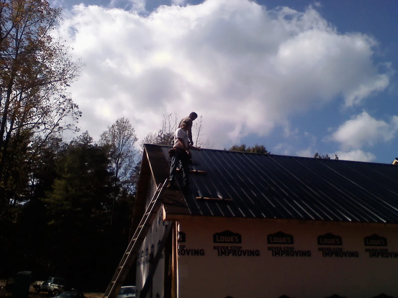 Roofer fastening dark metal panels high against a cloudy sky, from a Roof Inspection job in Wood River