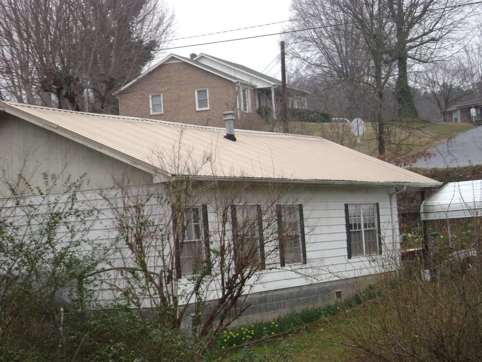 Tan metal roof on a white sided house set into a hillside — Commercial Roofing by Roofing Brothers in Wood River
